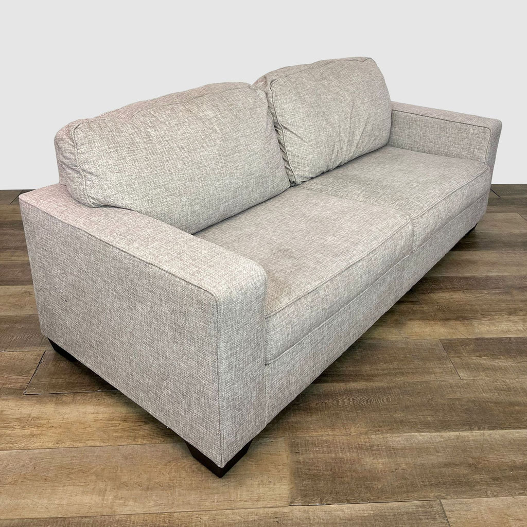 2. Side angle view of the Termoli loveseat by Ashley Furniture showing its blocked arms and sturdy wood feet on a wooden floor.