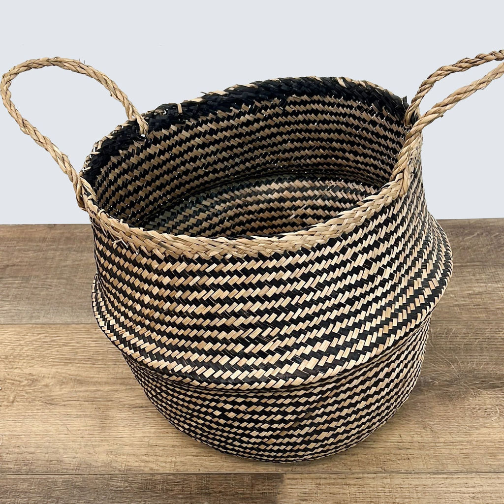 3. Round woven basket with two handles, featuring black and natural tan patterns, displayed on a wooden floor.