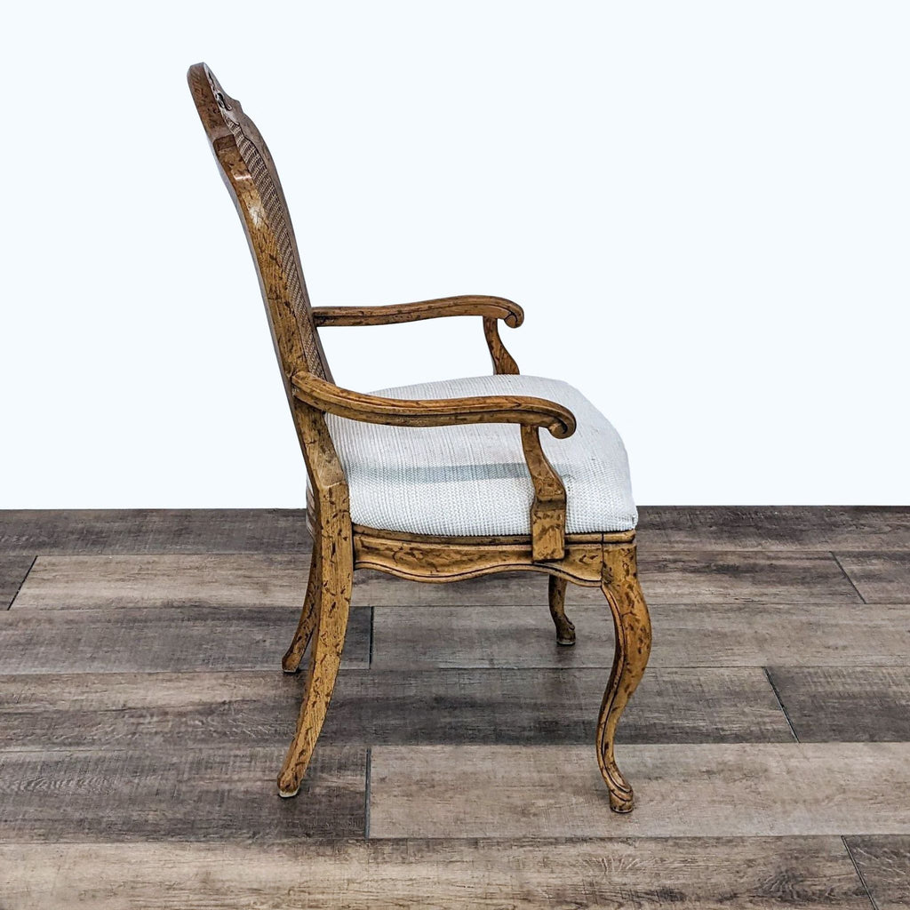 2. Side view of a Reperch Louis XV style wooden armchair with a cushioned seat and elegant curved lines on a wooden floor.