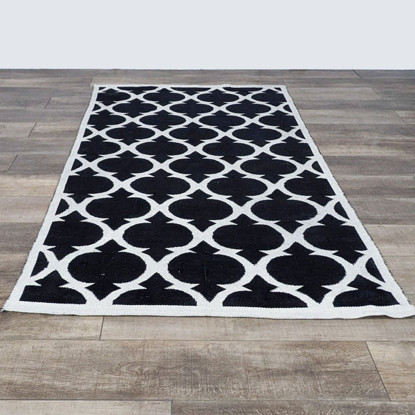 1. The Land of Nod 5'x8' black and white lattice pattern area rug laid out on a wooden floor.