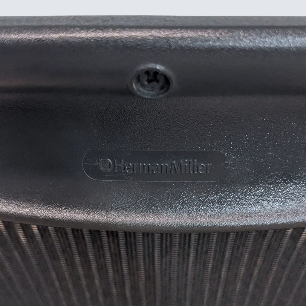 3. Close-up of the Herman Miller logo embossed on the back of a black Pellicle fabric suspension of an Aeron Side Chair.