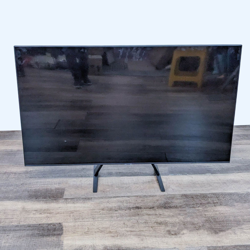 3. Off state Samsung flat-screen TV with a glossy black screen and slim design, showcasing its sleek aesthetic on a wooden floor background.