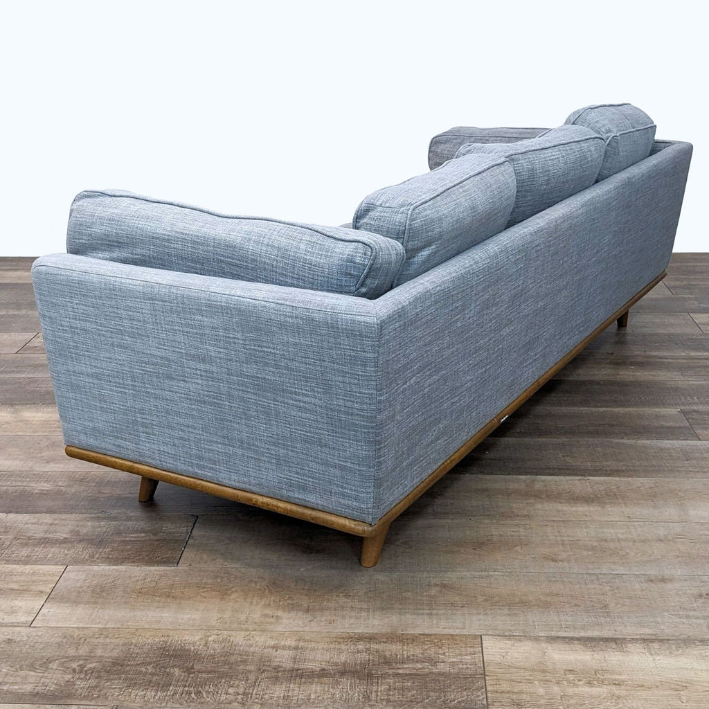 Rear view of a Article 3-seat sofa, featuring Mid-Century Modern style with light blue upholstery and wooden base, in room with wooden floor.