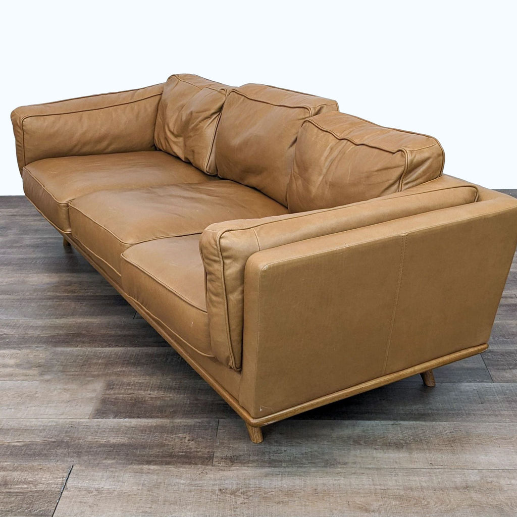 Angle view of the Timber sofa by Article, displaying the oak wood trim and feathery Charme Tan leather cushions.