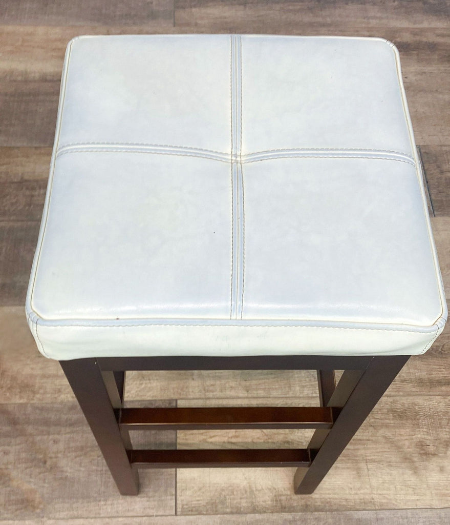 3. Close-up of a Reperch faux leather-upholstered stool with wooden legs, part of a compact dining set.