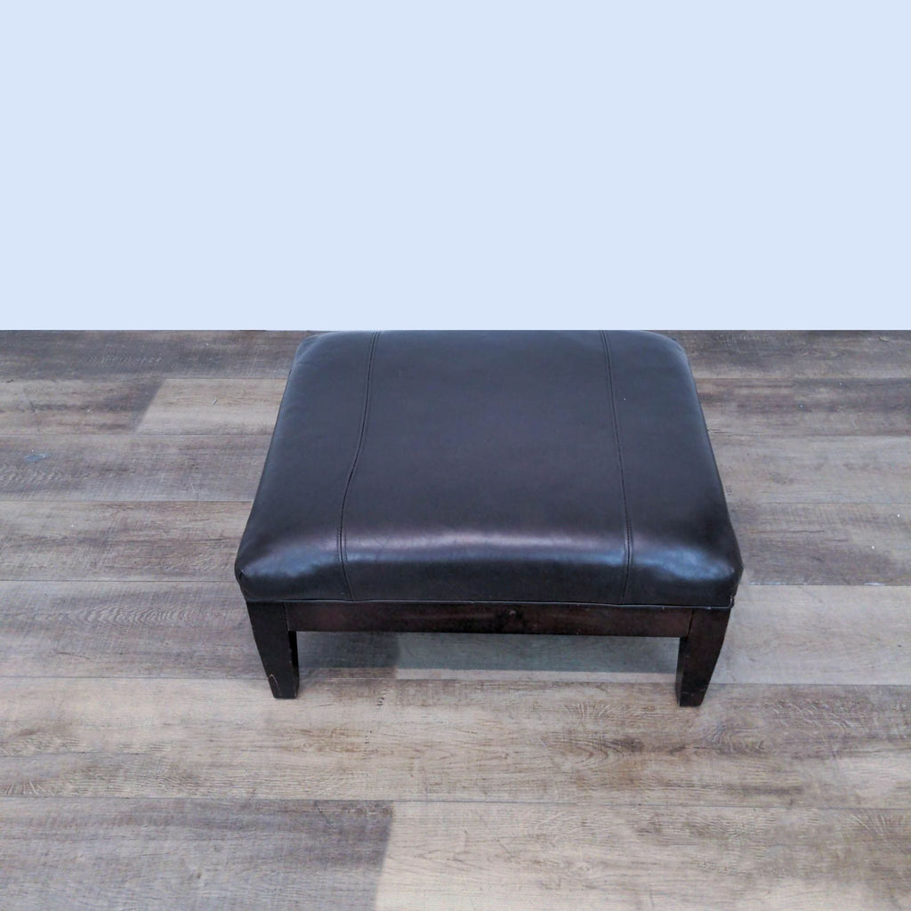 2. "Room And Board McCreary Modern dark finish solid wood framed ottoman with a padded brown leather top, shown on a wooden floor."