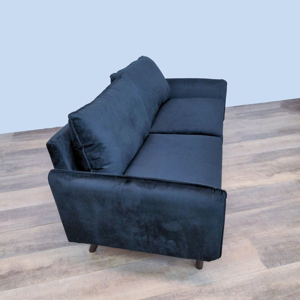 Side view of velvet upholstered loveseat with wooden legs.