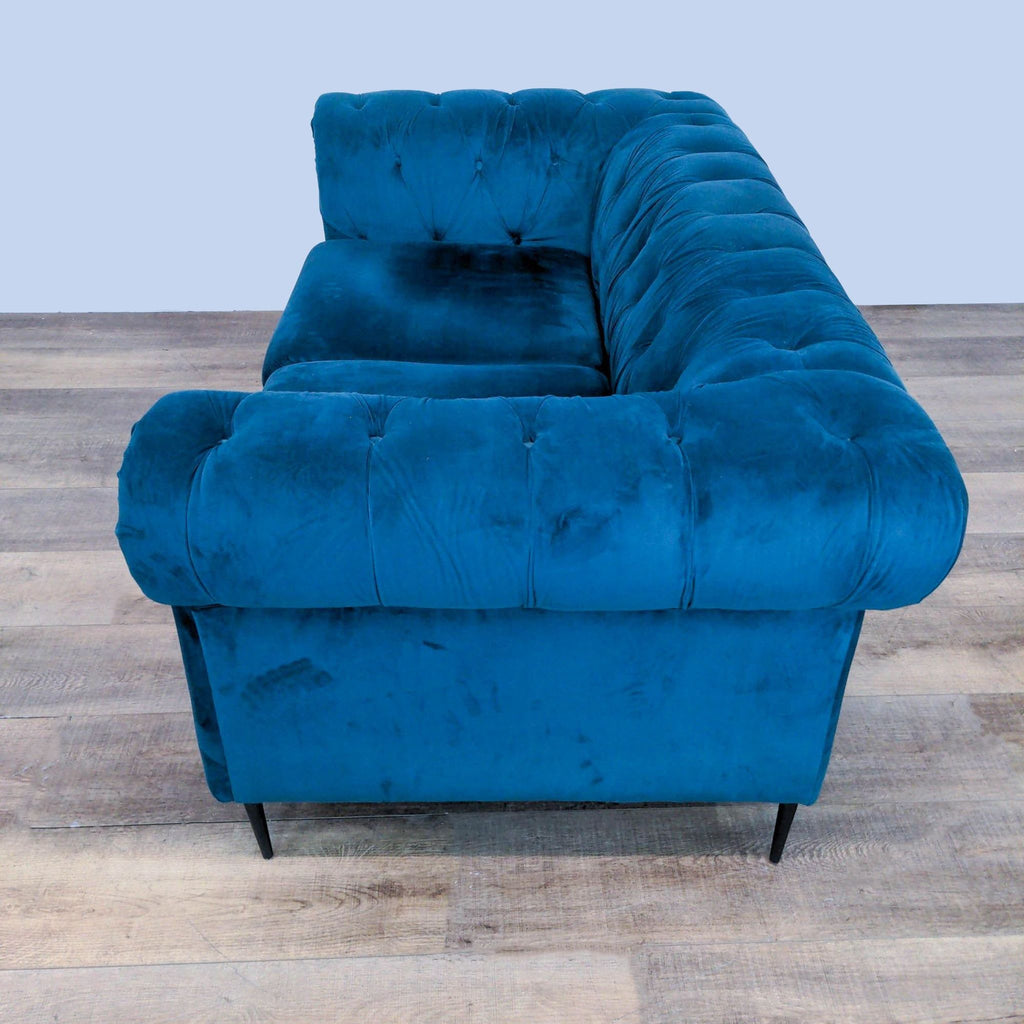 3. "Rear quarter view of a luxurious Reperch blue velvet loveseat with intricate tufting details and sleek legs."