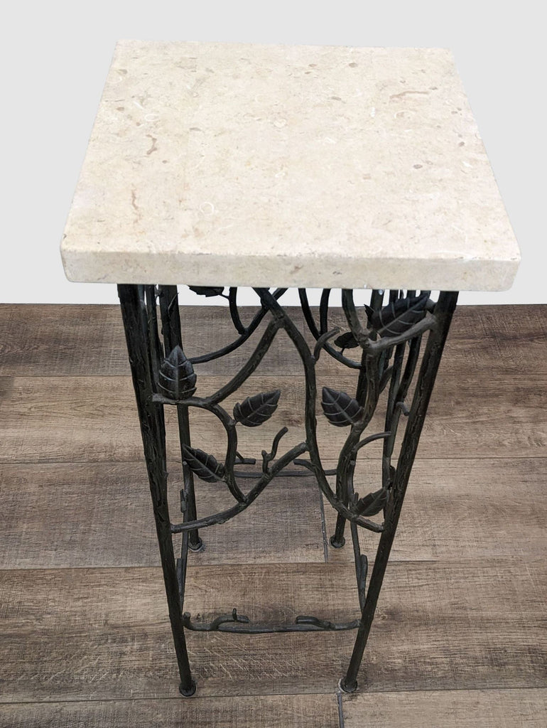 3. Decorative wrought iron Reperch table with leafy details and a beige stone tabletop on a wooden floor.