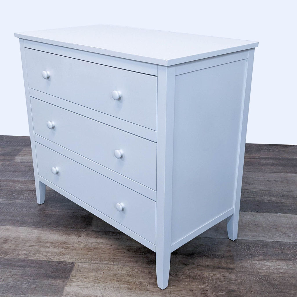 3. Side perspective of Pottery Barn Kids' white Emerson transitional dresser with three drawers, against a wood floor background.