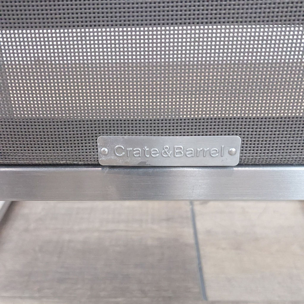 Close-up of Crate & Barrel logo on modern dining chair with weather-resistant mesh fabric.