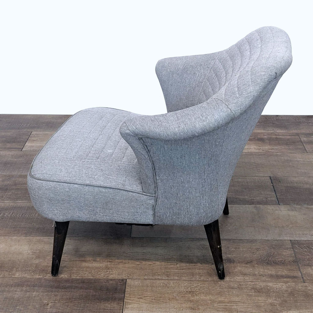 2. Side view of the Martin salon chair by HD Buttercup, featuring a gray wingback style with channel tufting and sleek, dark tapered wooden legs.