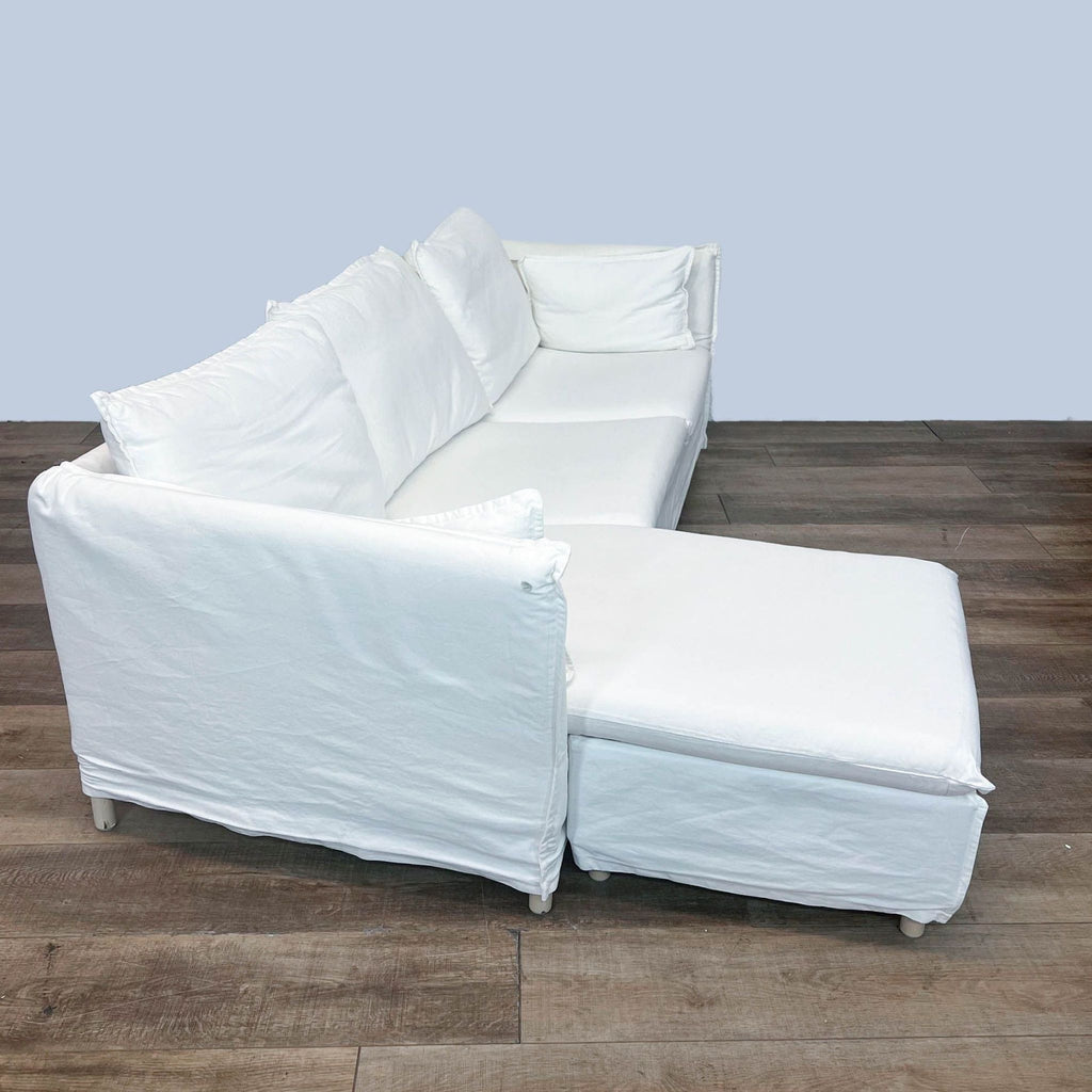 2. Side view of an Ikea white sectional sofa featuring a chaise lounge and white loose-fitting slipcover.