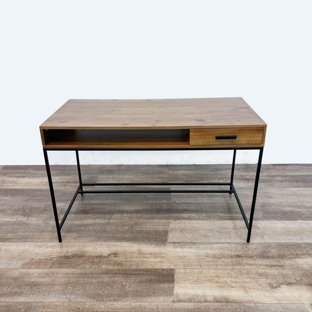 1. Frontal view of a modern Living Spaces wooden desk with a single drawer and metal frame on a wood-patterned floor.