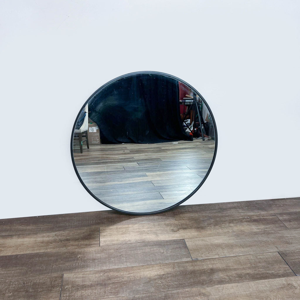 Williams-Sonoma round mirror with sleek metal frame standing upright on a wood-textured surface.