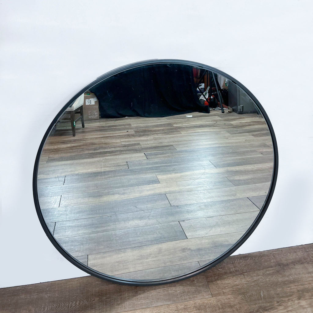 Round Williams-Sonoma mirror with metal frame on a wooden floor against a white wall.
