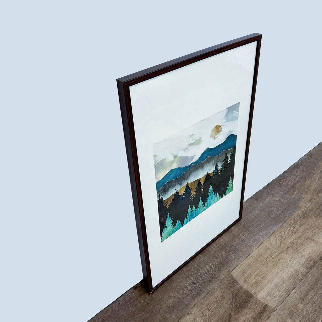 3. Angled view of a SpaceFrog painting of mountains and forest in a dark wooden frame, standing on a wooden floor.