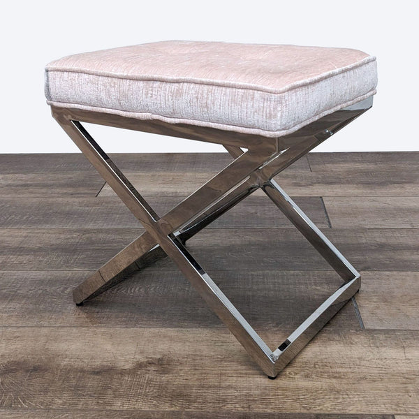 Light pink crushed velvet ottoman with chrome X-base by Pier 1 on wooden floor.