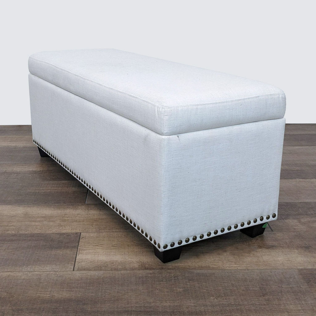 Linen look storage bench with closed lift top, nailhead accents, and dark finished feet by Living Spaces, against a wood floor.