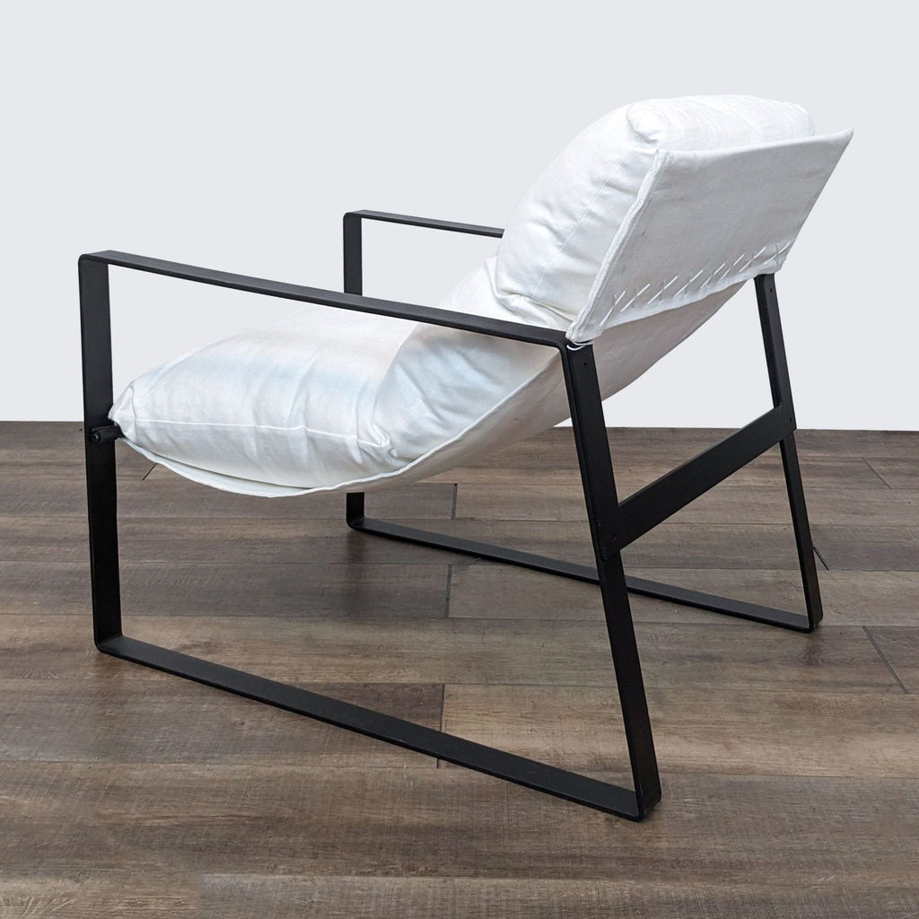2. Side view of a modern lounge chair with white linen upholstery and a distinctive black iron frame on a wooden floor.