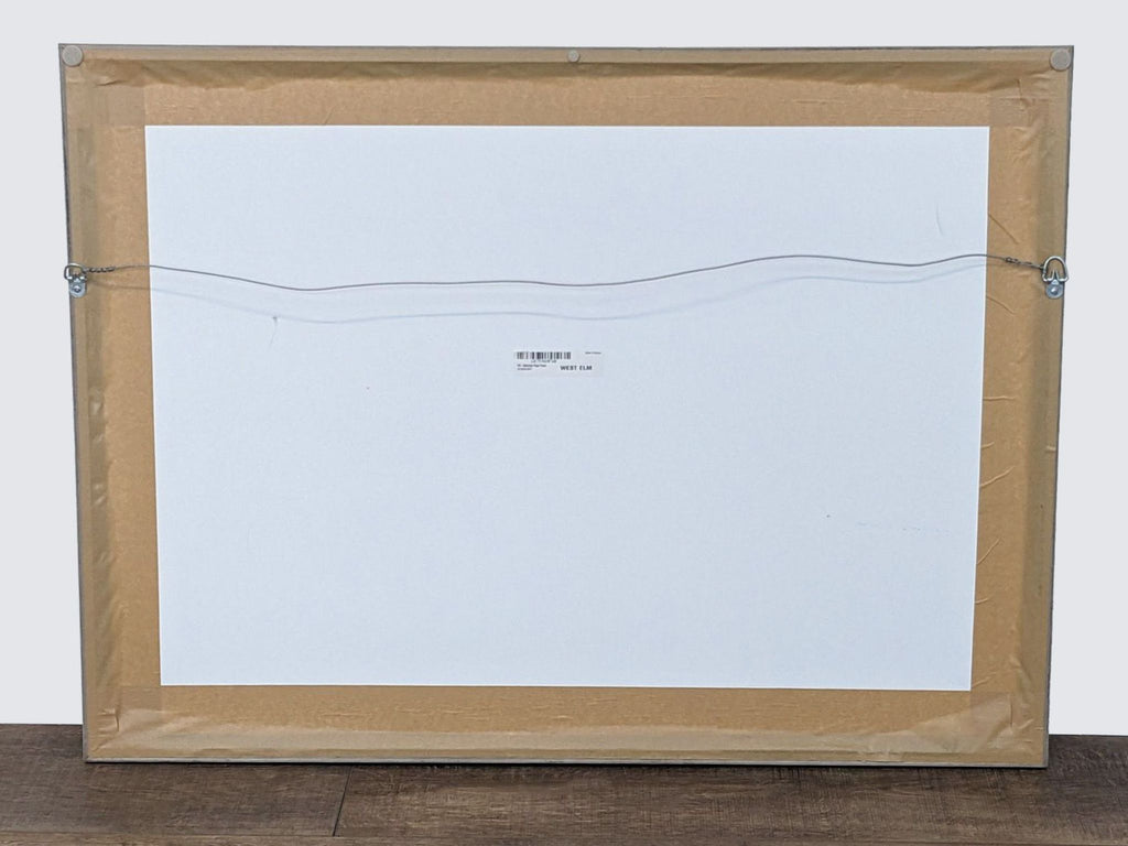 2. Back view of a West Elm framed photo print showing the wire for hanging and a paper backing.