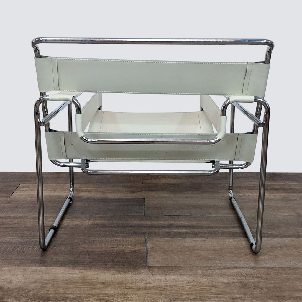 Side view of a Wassily lounge chair by Knoll featuring a tubular chrome frame and leather strapping on a wooden surface.