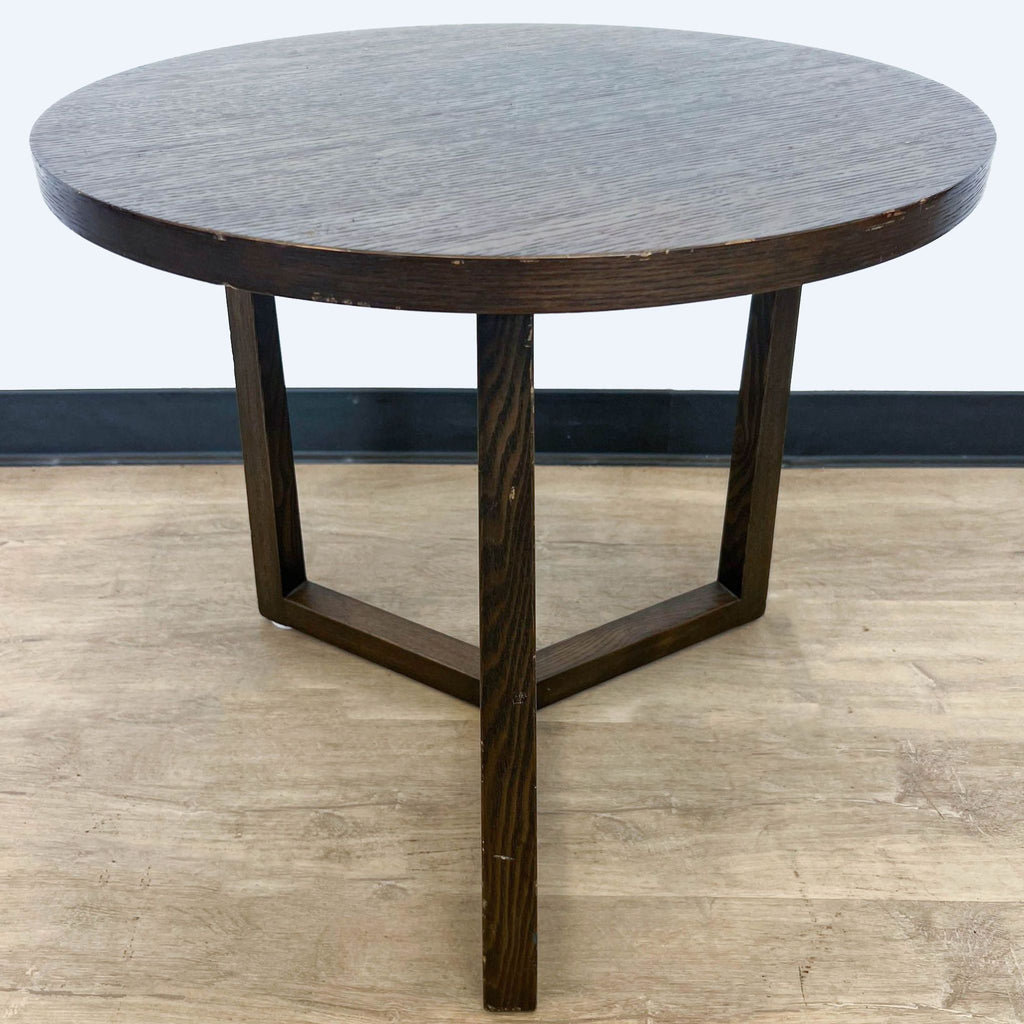 Circular wooden end table by Reperch with textured surface, against a gray wall and wooden floor.