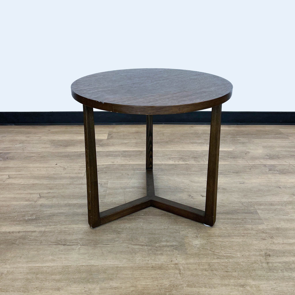 Dark-finished Reperch circular end table with sturdy triangular legs, on a light wood floor.