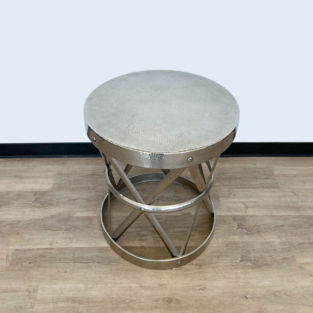 3. Metallic side table with a distinctive open X base structure by Reperch, against a black and white wall backdrop.