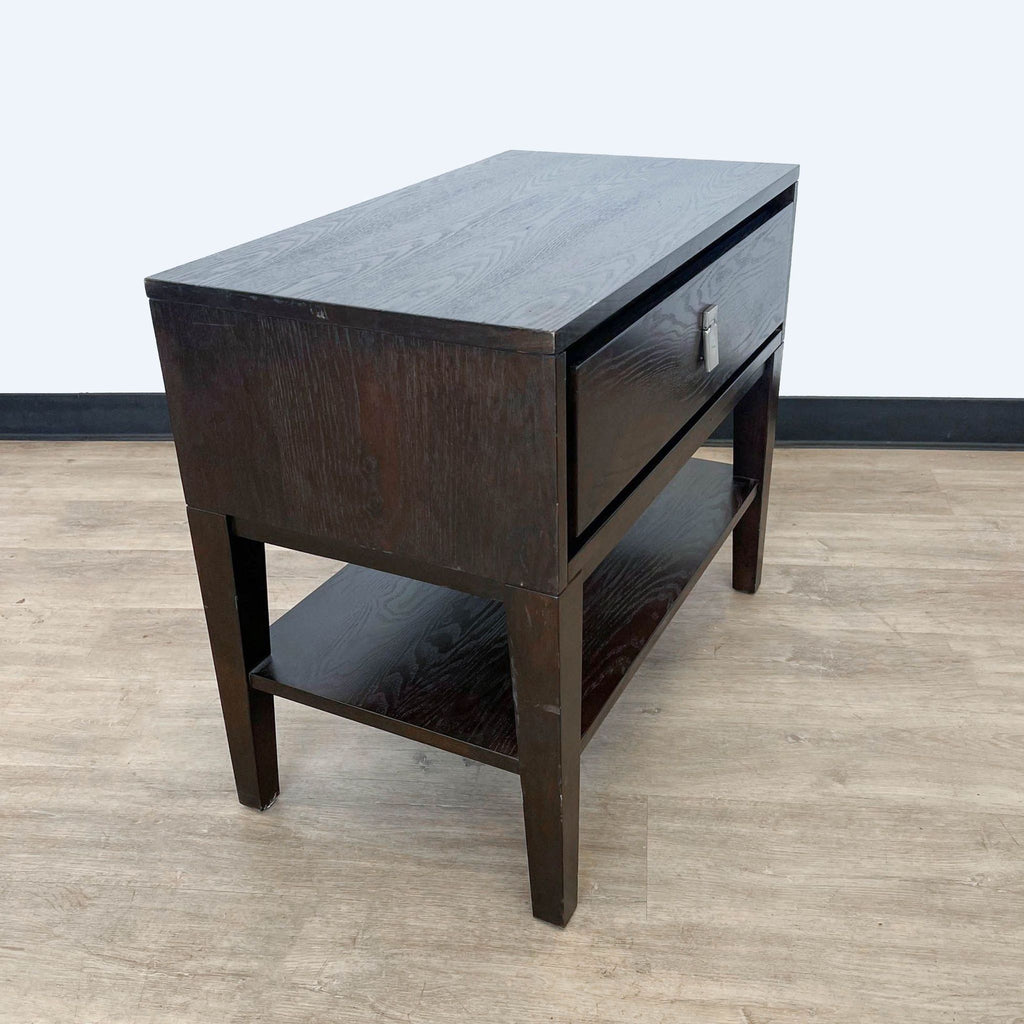Side view of a West Elm dark brown end table with a lower shelf, on light wood flooring and grey background.