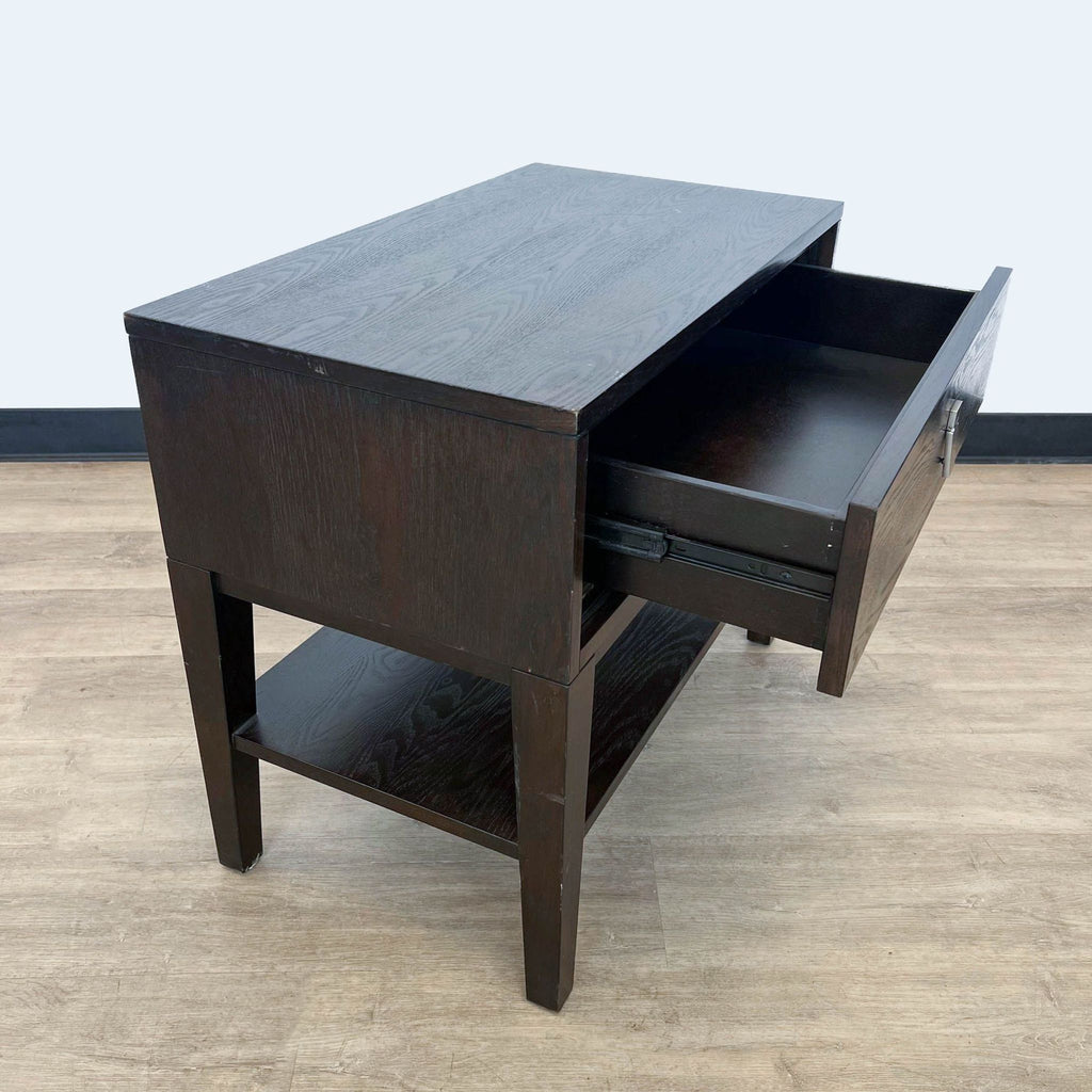 Dark wood West Elm end table with an open drawer, showcasing storage, against a grey wall and light flooring.