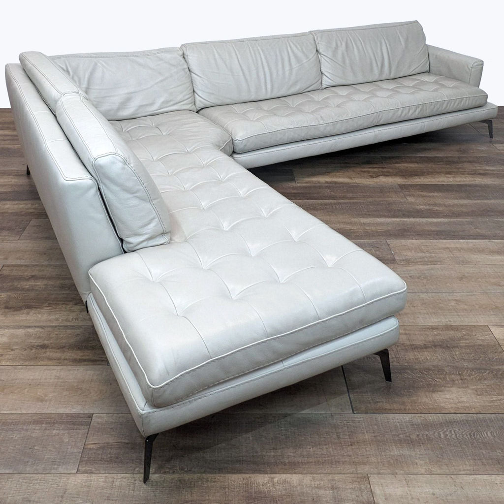 Modern Reperch Italian-made light grey leather sectional with chaise, tufting, and tapered legs on wooden floor.