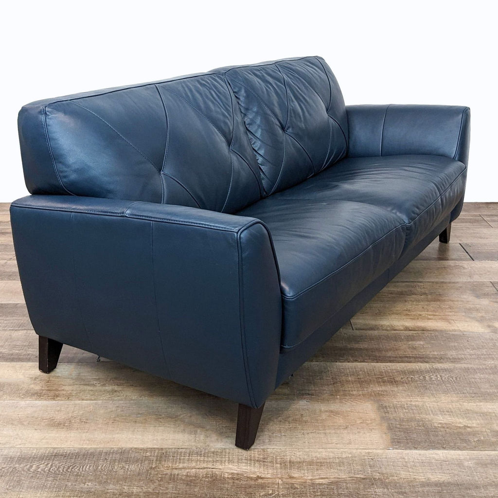 Angled view of the Miya loveseat from Macy's featuring flared arms and diamond-stitched tufted back in navy blue.