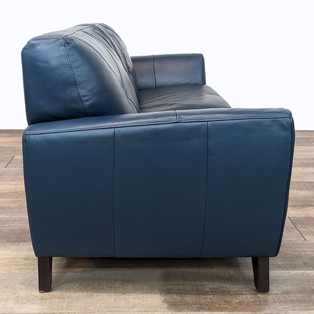 Side view of Macy's Miya navy blue loveseat showing tapered wooden legs and smooth leather upholstery.