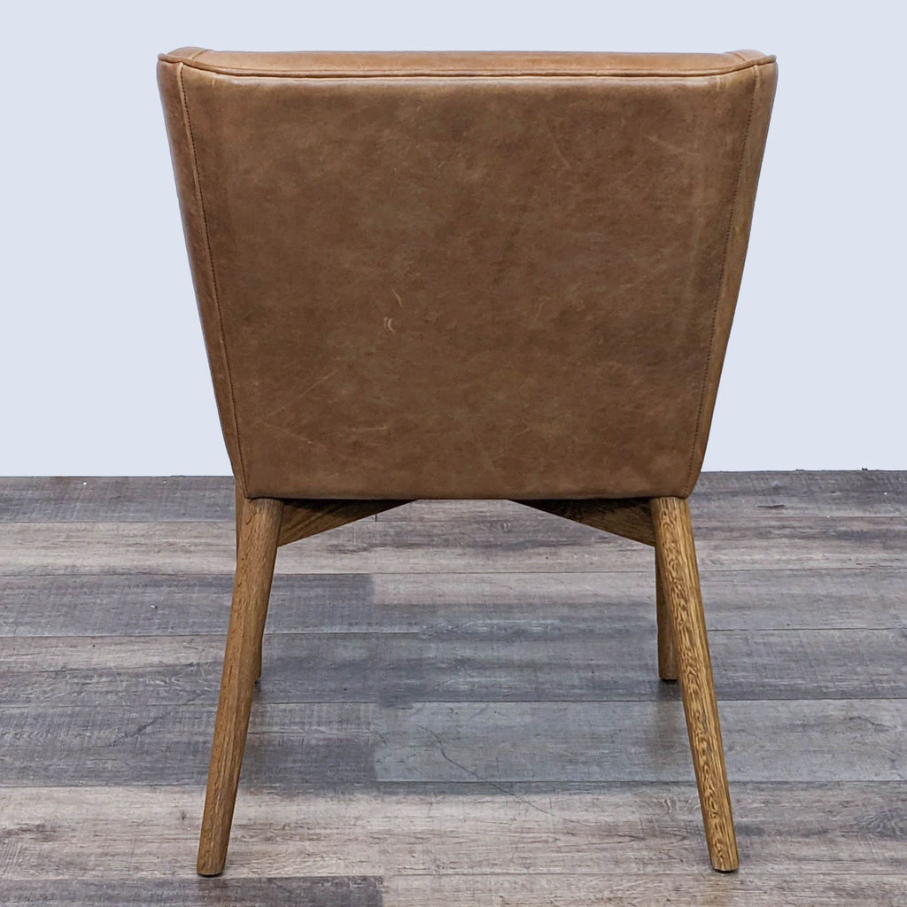 Rear view of a brown leather lounge chair, emphasizing its smooth, curved design and wooden legs.