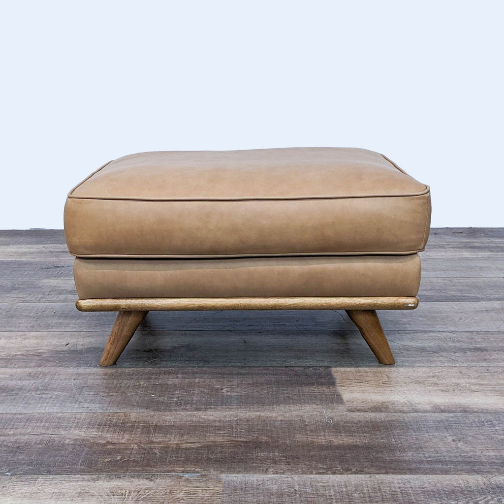 Mid-Century leather ottoman with foam cushion on wooden slant legs.