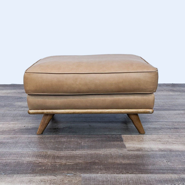 Mid-Century leather ottoman with foam cushion on wooden slant legs.