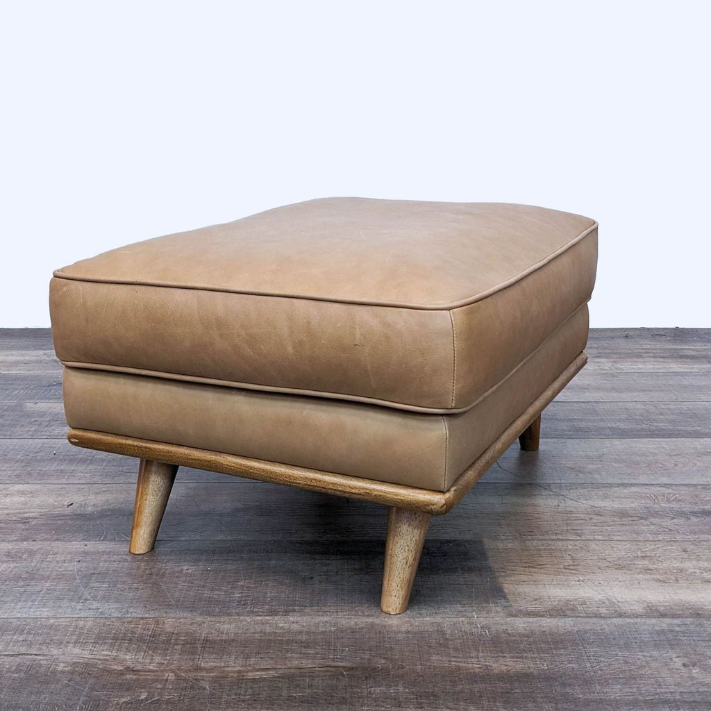 Side view of leather ottoman with wooden legs and plush cushion.