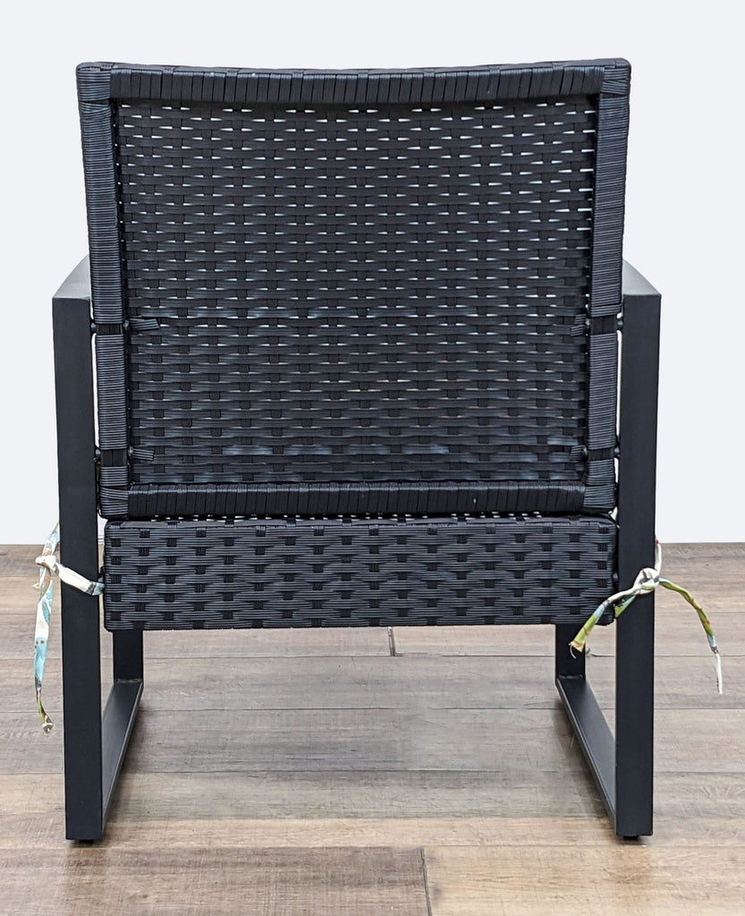 Rear view of a black wicker armchair by Reperch with a vivid floral back cushion.