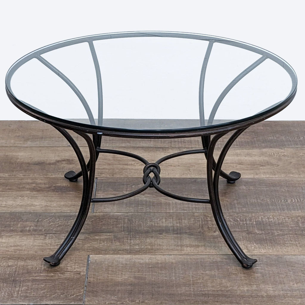 2. "Round glass-top coffee table with an ornate wrought iron base on a wooden floor, by Pier 1 Imports."