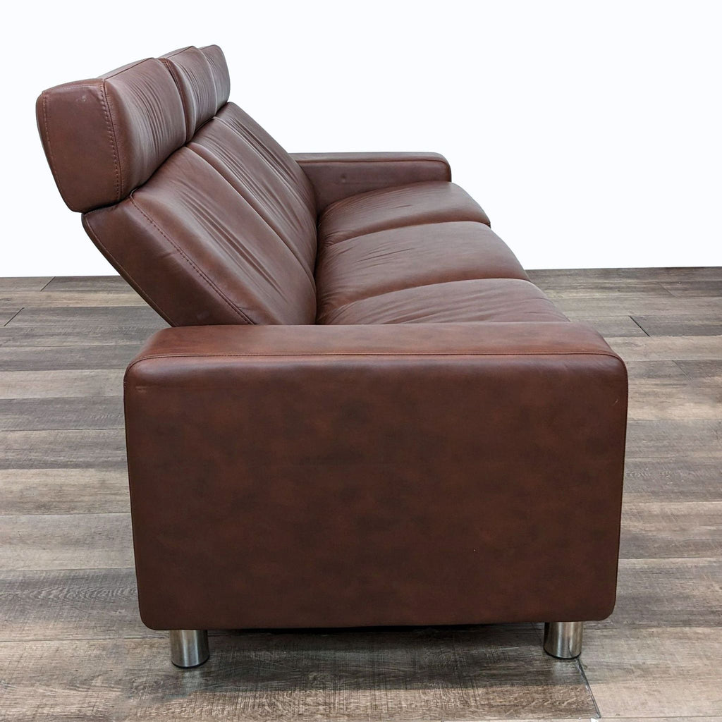 2. Side view of a dark brown leather upholstered 3-seat sofa with high backs and metallic legs on a wooden floor.