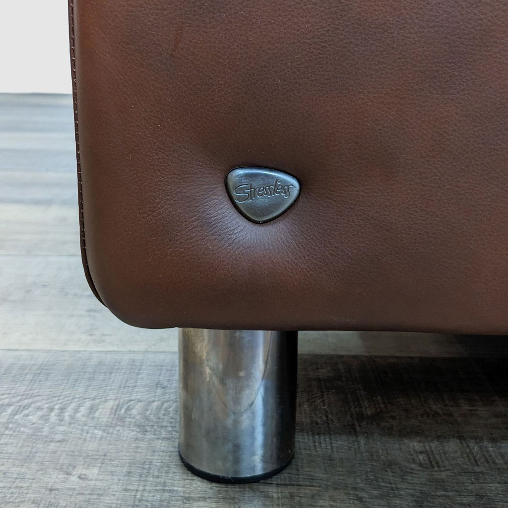 3. Close-up of a Stressless logo on the side of a leather 3-seat sofa with a metal leg, showcasing the brand detail.