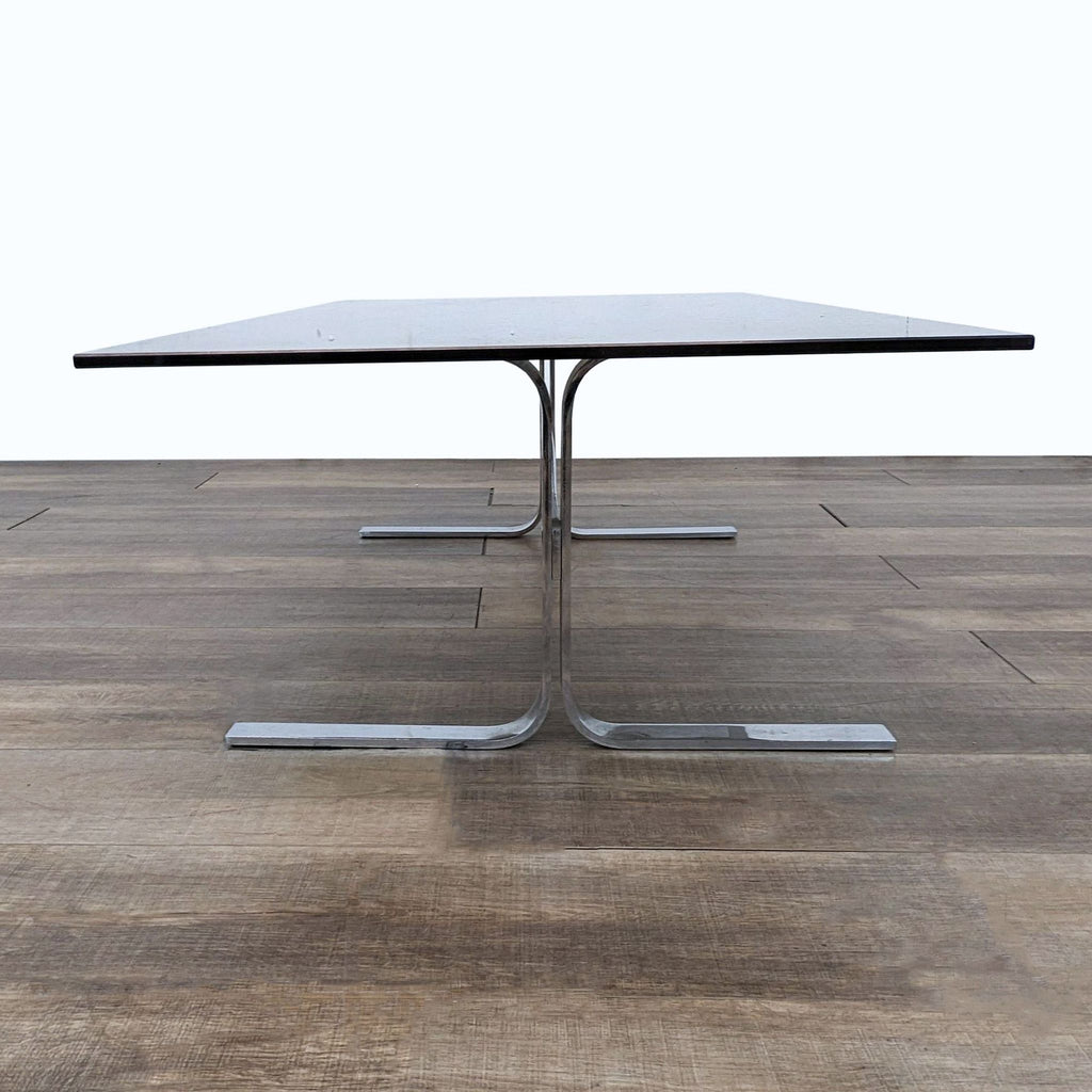 Elevated view of a Reperch coffee table, displaying its dark surface and distinctive trestle stainless base.