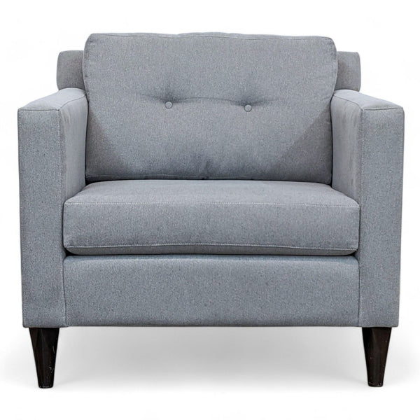- Front view of a Reperch contemporary grey fabric armchair with cushioned seat and dark wooden legs.