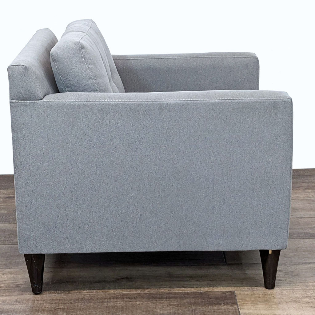 Side view of a contemporary grey armchair showing armrests and legs.