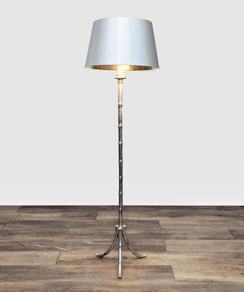 John-Richard Mid Century brass floor lamp with a triform base and grey drum shade, in a room with wooden flooring.