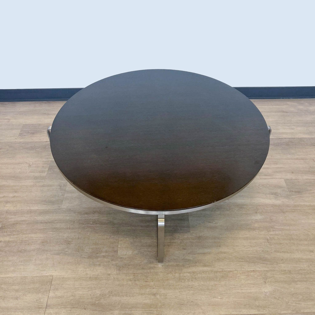 3. "Elegant round coffee table from Reperch with a dark wood finish top and a shiny metallic base, on a laminate floor."