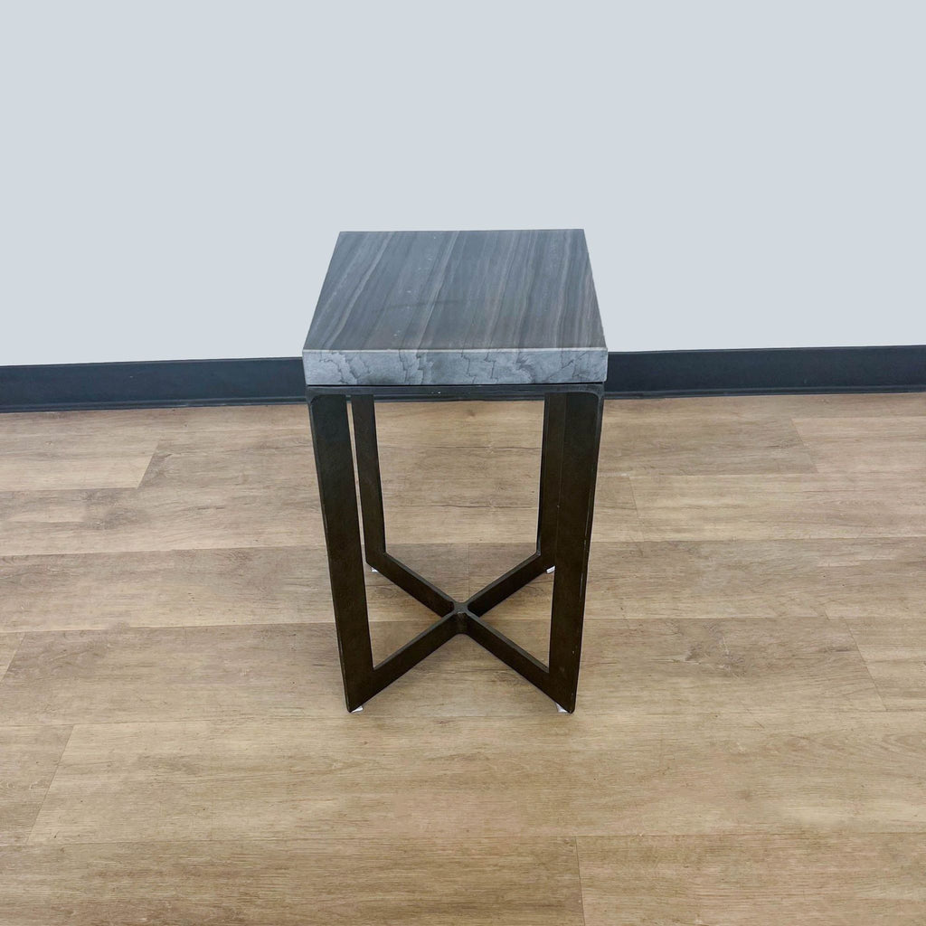 A square marble-topped Reperch console table with sturdy crisscross metal legs on a wooden floor.