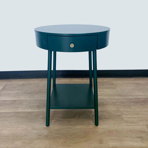 Alt text 1: Round dark teal end table by Reperch with a drawer and lower shelf, set against a light wood floor and grey wall.