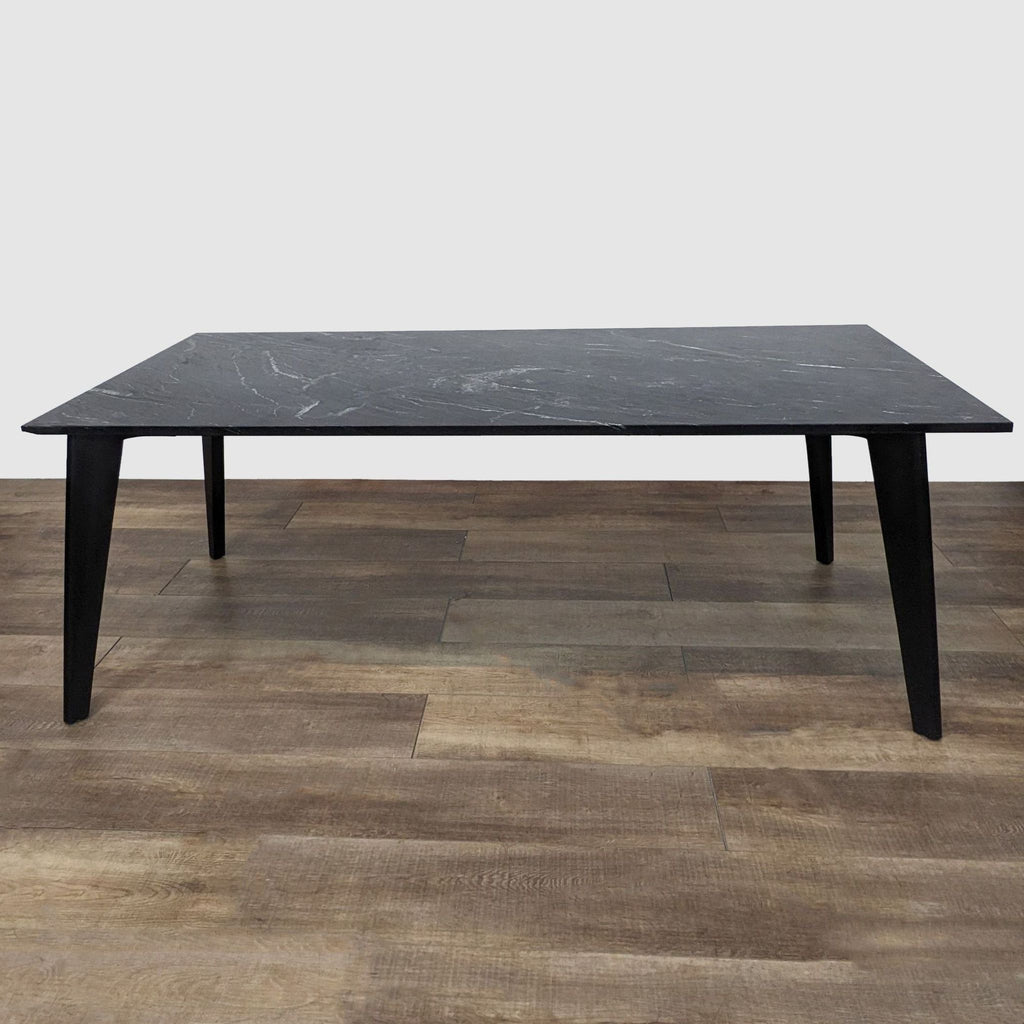 Harper Dining Table by CB2 with black steel angled legs and black marble top with grey veining on wooden floor.